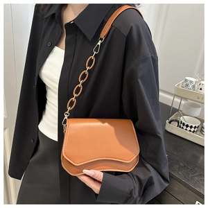 Detail of a brown leather shoulder bag with a unique wave-shaped flap and metal chain strap