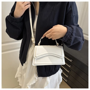Close-up of a white minimalist handbag featuring a geometric fold flap and top handle