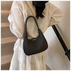 Detail of black crescent hobo bag with grid texture and gold metal chain strap on model