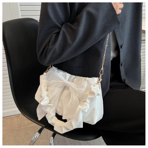 Close-up of elegant white bow handbag with ruffled handle and gold chain strap detail
