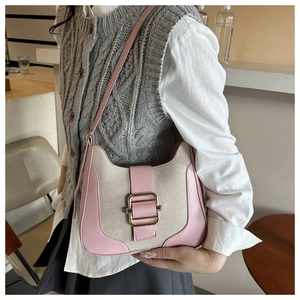 Detail of pink leather trim and gold buckle on a canvas shoulder bag shown in use