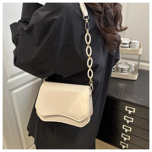 Detail view of cream wave-flap crossbody bag with chic chain strap on a model