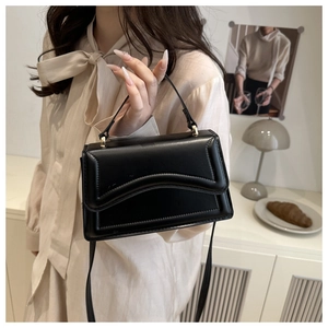 Détail d'un sac à main noir minimaliste au design ondulé porté par un mannequin