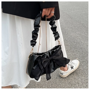 Detail of black crossbody bag featuring a large bow and pleated leather handle