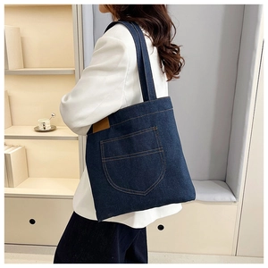 Detail of blue denim tote bag with decorative stitching and brown leather label accents