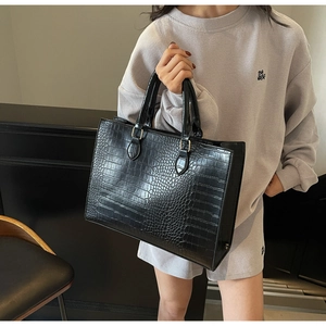 Detailed side view of black crocodile pattern tote bag held by a model in gray sweatshirt
