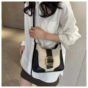 Detail view of the beige canvas tote with black leather trim and gold metal buckle strap