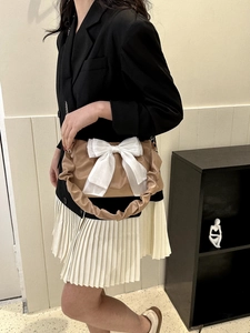 Detail of khaki pleated strap bag featuring a large white bow decoration and chain
