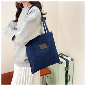 Detail of blue denim tote bag with brown leather patch on casual street style model