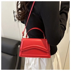 Détail d'un sac bandoulière rouge matelassé avec bords ondulés et boucles dorées sur modèle