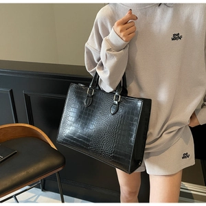 Detail of black crocodile pattern tote bag featuring metallic handle buckles and texture