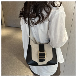 Detail view of canvas saddle bag with black leather trim and golden metal clasp on shoulder