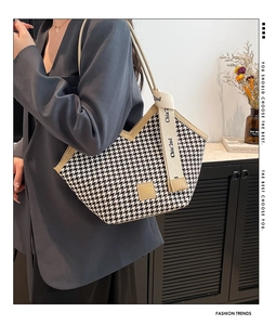 Detail of houndstooth tote bag with beige edges and lettered strap shown on a shoulder