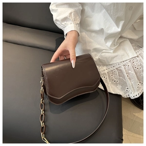 Close-up of wavy flap edge and resin chain detail on a dark brown underarm bag