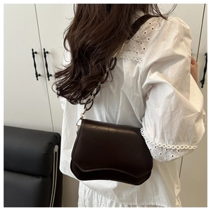 Detail of dark brown leather bag with wavy flap and gold chain strap on shoulder