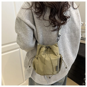 Detail of an olive green drawstring bucket bag with mesh side pocket and wide strap