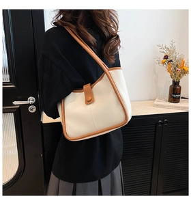 Detail of cream tote bag with brown leather trim and decorative snap strap on a model