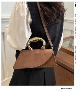 Detail of artistic wavy gold metal handle and dual-texture leather on brown handbag