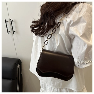 Close-up of minimalist dark brown underarm bag featuring a gold chain and oval ring strap