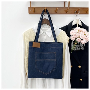 Detail der blauen Denim-Tragetasche mit braunem Lederetikett in Lifestyle-Umgebung