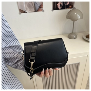 Detail of minimalist black leather underarm bag featuring a gold buckle and chain strap