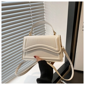 Détail d'un sac à main crème avec rabat matelassé ondulé et ferrures en métal doré brillant