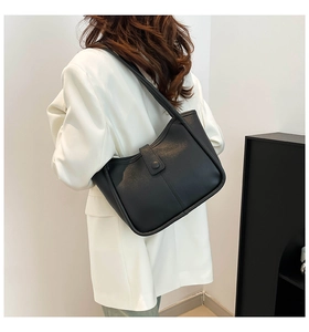 Minimalist black leather tote bag shown on shoulder in a modern lifestyle setting