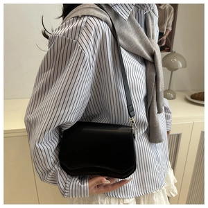 Close-up of black crossbody bag with unique wave bottom design on model