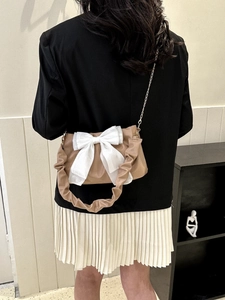 Detail of khaki shoulder bag featuring a large white tulle bow and gold chain strap