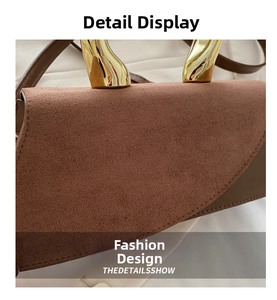 Detail of brown suede square bag with arched gold metal handle on white fabric