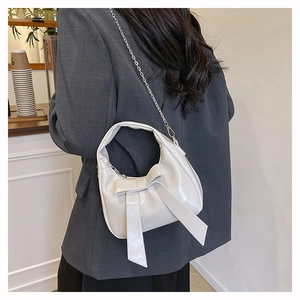 Detail of white semi-circular handbag with bow decoration and silver chain strap