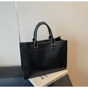 Detail of black crocodile embossed tote bag with glossy leather texture and metal buckles