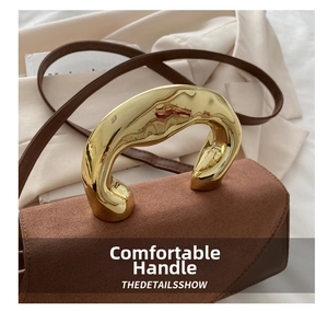 Detailed macro view of brown leather handbag with luxury gold wave-shaped metal handle