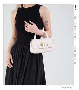 Detail of a creamy beige square handbag featuring a stylish round gold metal lock clasp