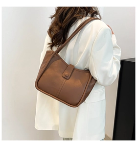 Brown leather bucket bag styled as a shoulder bag on a model wearing a white blazer