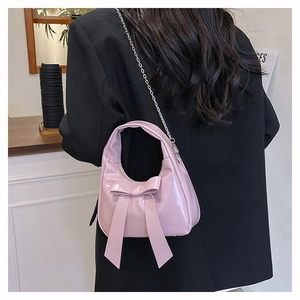 Detail of pink glossy bow crossbody bag with metallic chain strap worn by a model