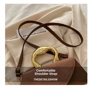 Detail of brown leather tote with unique wavy gold metal handle and slim shoulder strap