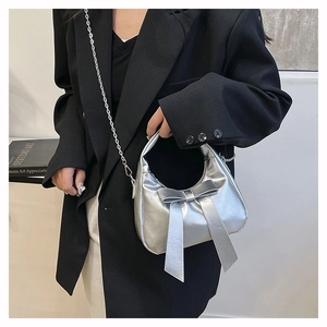 Detail view of a silver metallic bow handbag with sleek chain strap and glossy finish