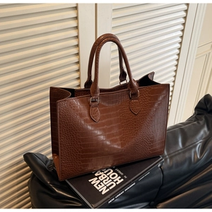 Close-up of brown crocodile texture tote bag with double handles in a modern urban setting