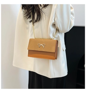 Close-up of caramel shoulder bag with woven texture, leather, and golden bow detail