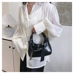 Detail of a black glossy leather bucket bag featuring a large bow and silver chain strap