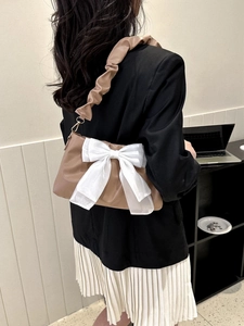 Detail of a brown shoulder bag with a large white organza bow and pleated strap design