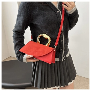 Détail d'un sac à main rouge avec poignée dorée artistique sur un pull gris