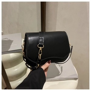 Detail of black faux leather saddle bag featuring gold metal buckle and accent chain