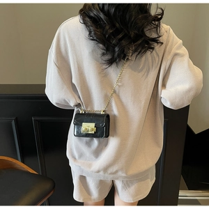 Detail of a black mini flap crossbody bag with gold metal lock and chain strap on model