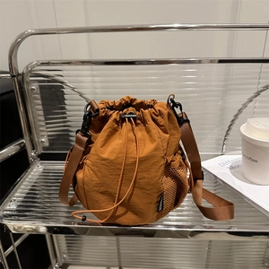 Brown nylon drawstring bucket bag with mesh pocket and fashion label on display