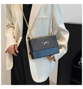 Detail of contrast crossbody bag featuring golden bow metal accent and chain strap