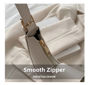 Close-up of smooth gold zipper and hardware on a minimalist cream shoulder bag