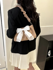 Detail of a brown PU leather shoulder bag with a large white organza bow and ruched strap