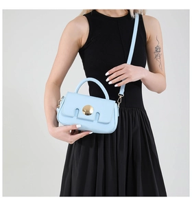 Detail of light blue crossbody bag with gold round buckle and geometric flap texture